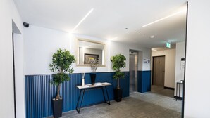 A modern reception area with a reception desk, two potted plants, a mirror, and a sign indicating the floor level. - Avenir Court Flat 5 (Finchley) (Greater London)