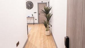 A hallway with a wooden floor, a clock on the wall, and a potted plant. - Avenir Court Flat 15 (Finchley) (Greater London)