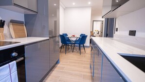 A modern kitchen with a dining area, featuring a large island, blue chairs, and a minimalist design. - Avenir Court Flat 15 (Finchley) (Greater London)