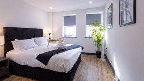 Una habitación de hotel moderna con una cama grande, mesitas de noche, una planta en maceta y cuadros en las paredes.