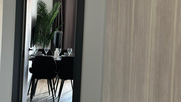 Un comedor moderno con un espejo de marco oscuro, una mesa de comedor con sillas y una planta en maceta.