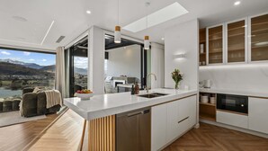 Une cuisine moderne dotée d’un grand îlot central, d’appareils électroménagers intégrés et offrant une vue sur un lac et des montagnes.