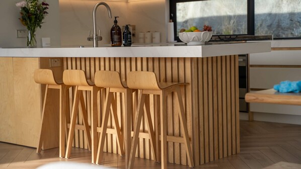 A modern kitchen with a white countertop, a built-in sink, and three wooden bar stools.