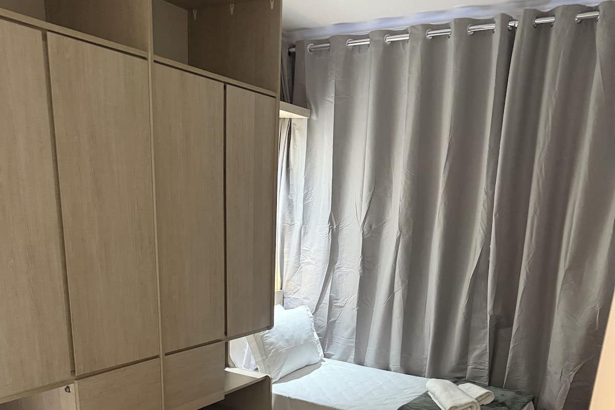 A room with a bed, a wardrobe, a small table, and a window with curtains.