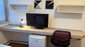 Une chambre à coucher de taille réduite, comprenant un lit, un bureau avec un ordinateur, un petit réfrigérateur et une chaise.