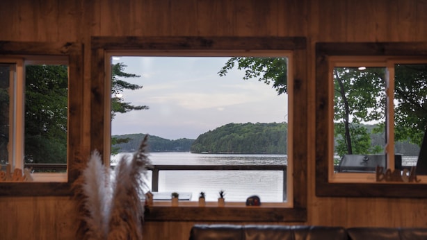 Ett rum med utsikt över en sjö och kullar, träväggar, en lädersoffa och en dekorativ fjäder.