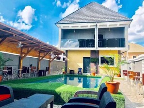 A two-story building with a swimming pool in front, surrounded by outdoor seating and a pergola. - Zara Max Hotel and Suites (Awka)