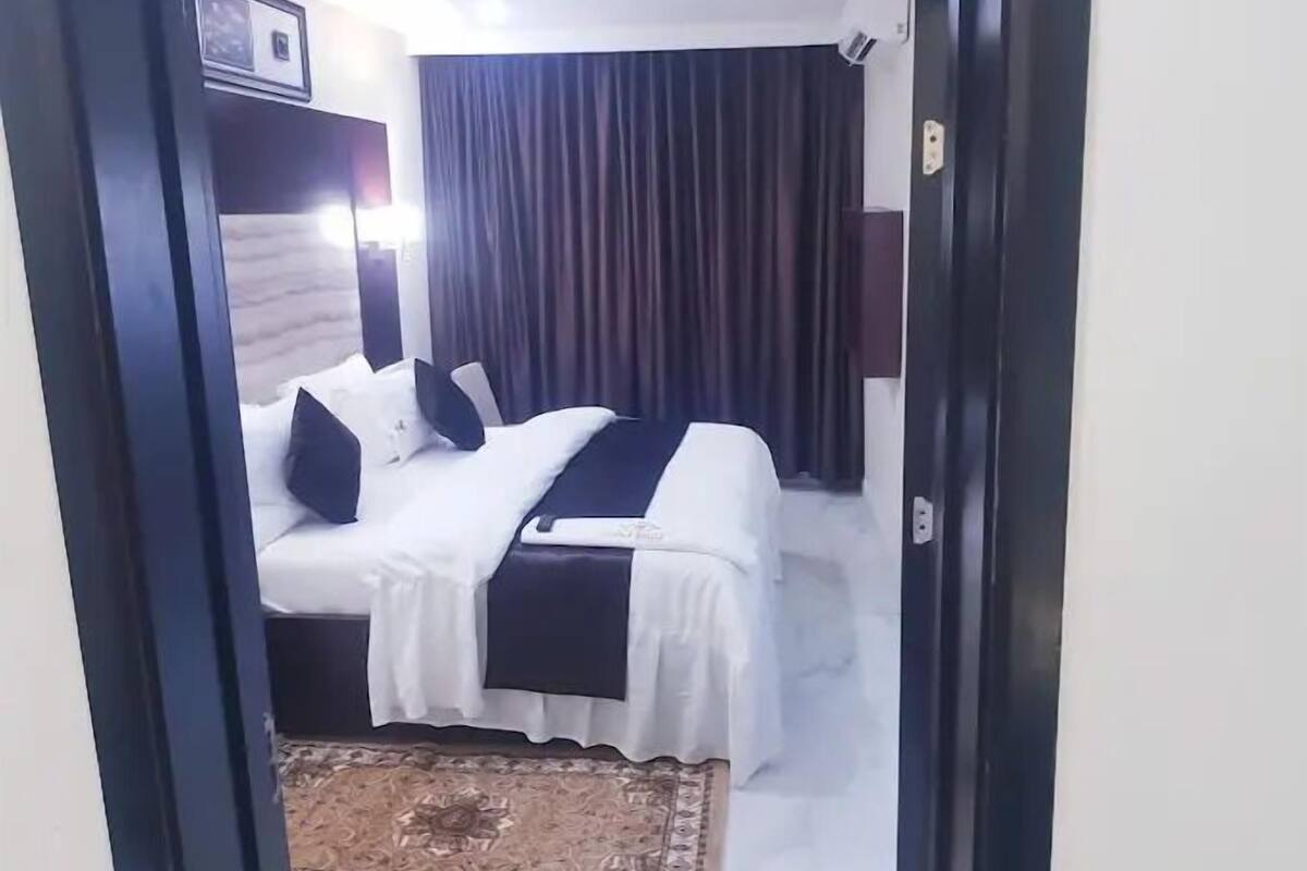 A hotel room with a bed, a bedside table, a lamp, and a window with curtains.