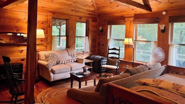 A cozy cabin interior with wooden walls and ceilings, a sofa, a chair, and a table. - Creekside B&B Cabin – Breakfast Included – Award-Winning Appalachian Farm (Irvine)
