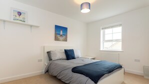 Une chambre à coucher avec un lit, une table de chevet, une fenêtre et un tableau accroché au mur.