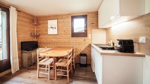 A compact kitchen with wooden walls, a dining table, chairs, a TV, and a small window.