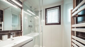 A modern bathroom with a glass-enclosed shower, a large mirror, and a window with lace curtains.