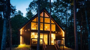 A wooden cabin with a large glass front, wooden deck, and stairs leading up to the entrance. - #1 Passionflower at Lost Forest Cabins (Richards)