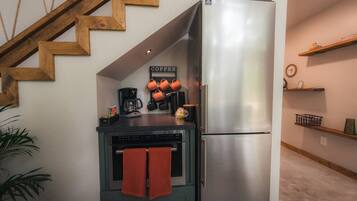 A compact kitchen with a stainless steel refrigerator, a coffee machine, and a stove.