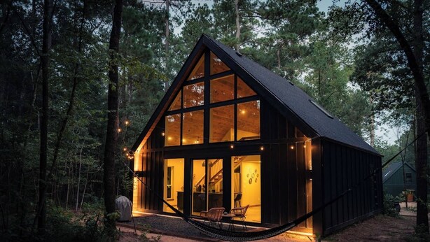 Une cabane dotée de grandes fenêtres, d’un hamac et d’une façade en bois.