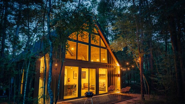 A modern log cabin with large glass windows, a dining area, and a cozy seating space. - #5 Woodpecker at Lost Forest Cabins (Richards)