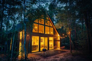 Une cabane en rondins moderne, dotée de grandes fenêtres en verre, d’un coin repas et d’un espace salon confortable.