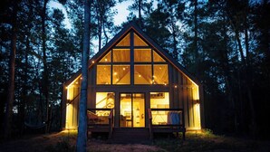 A wooden cabin with large windows, a deck, and a staircase leading to the upper floor. - #6 Turkey Tail at Lost Forest Cabins (Richards)
