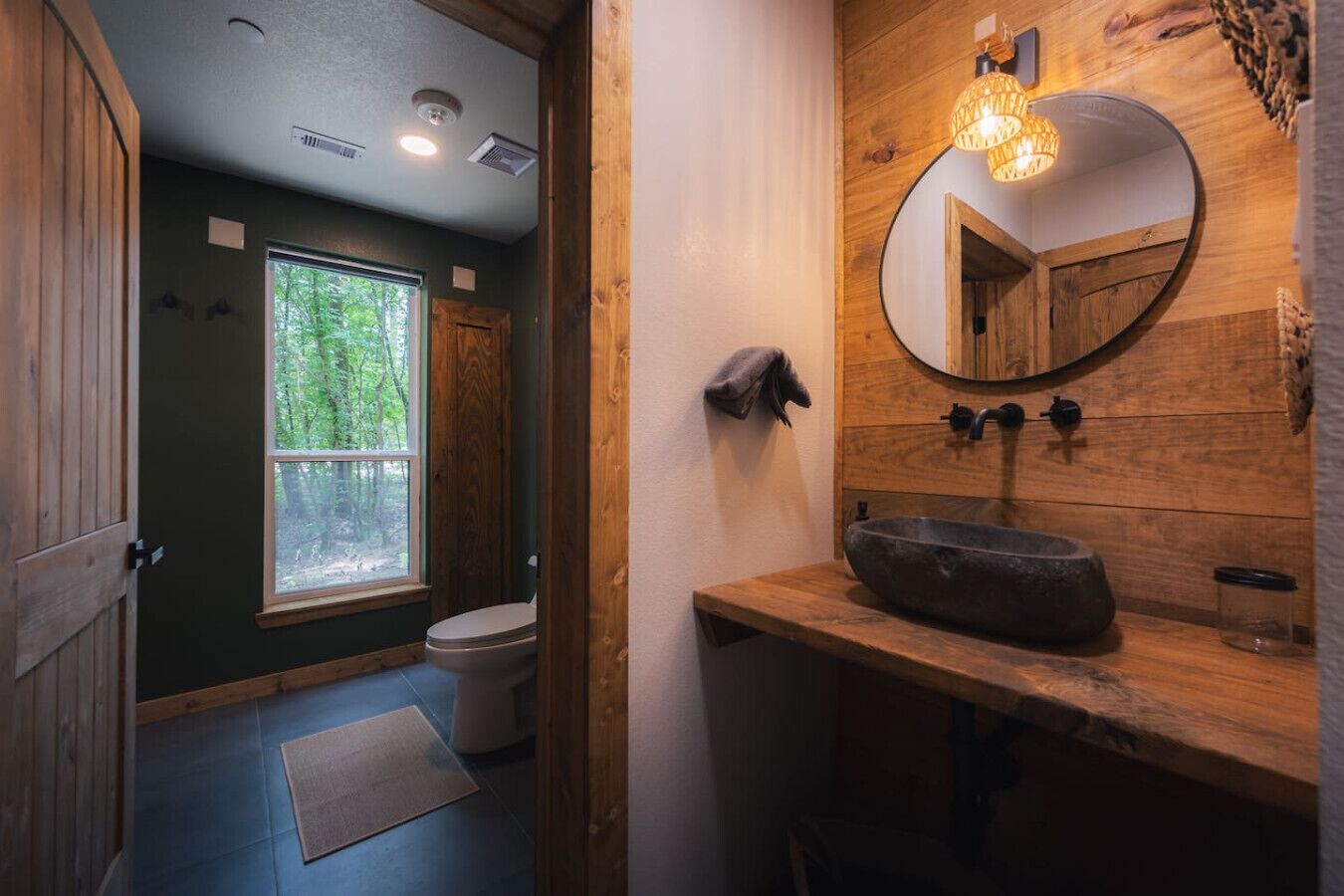A rustic bathroom with a wooden vanity, a round mirror, and a large window.