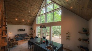 A spacious kitchen with a large island, wooden ceiling, and large windows offering a view of the outdoors. - #7 Beauty Berry at Lost Forest Cabins (Richards)