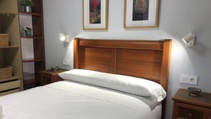 A neatly made bed with a wooden headboard, a bedside table with a bowl, and a shelf with baskets. - 14A11 Apartment with Views in Lastres by R2R (Lastres)