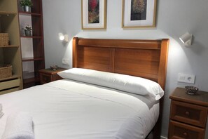 A neatly made bed with a wooden headboard, a bedside table with a bowl, and a shelf with baskets. - 14A11 Apartment with Views in Lastres by R2R (Lastres)