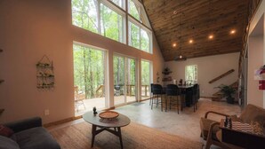 Uma sala de estar ampla com pé direito alto, grandes janelas e uma área de jantar com banquetas.