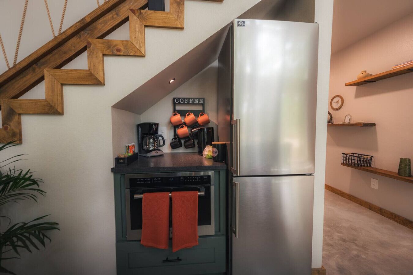 A compact kitchen with a stainless steel refrigerator, a coffee machine, and a stove.