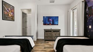 Ein Hotelzimmer mit zwei Betten, einem Fernseher an der Wand, einem Schminktisch und einem Poster.