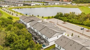 Un complesso residenziale moderno con un lago centrale, un'area parcheggio e una strada che conduce agli edifici.