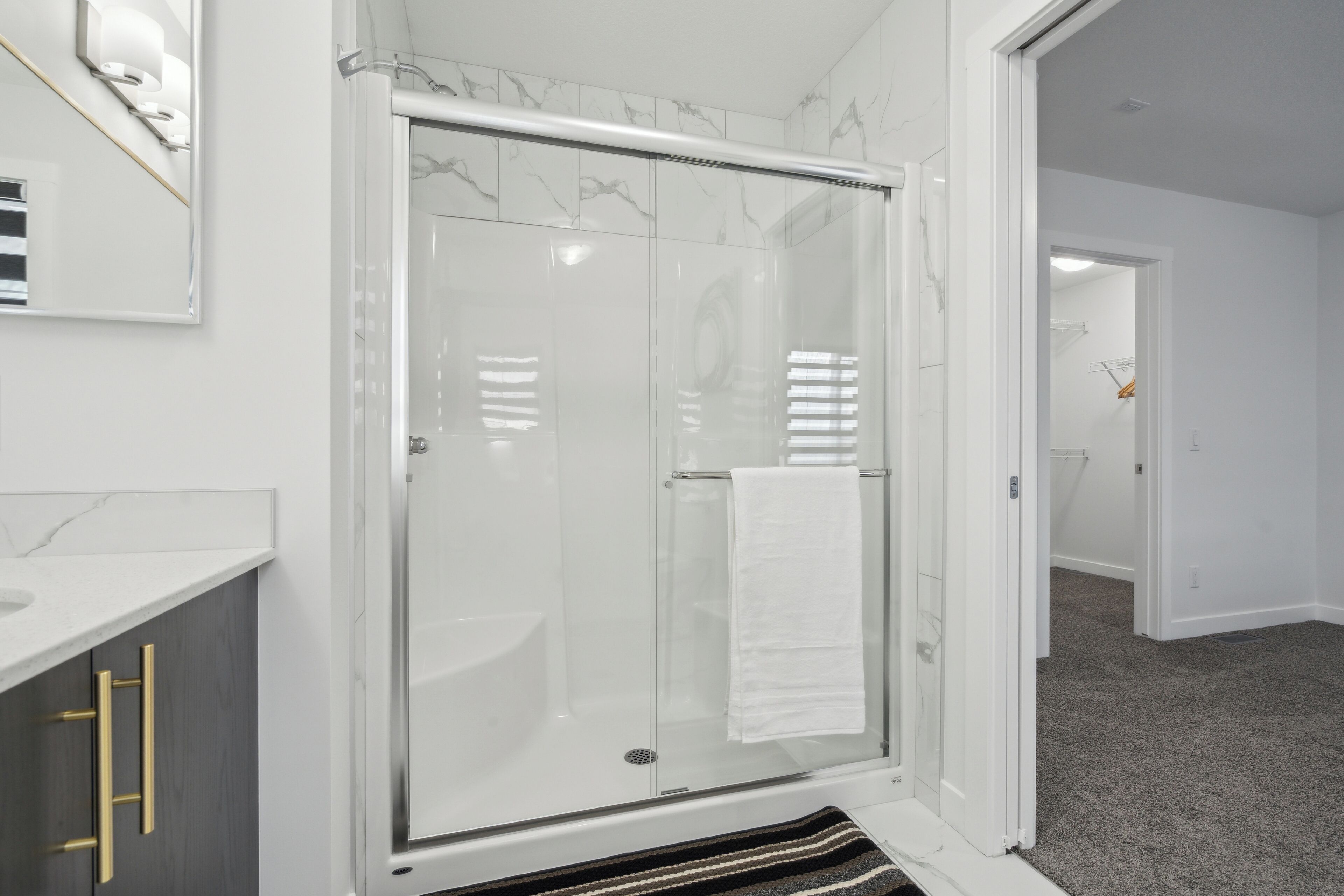 Une salle de bain moderne avec une douche à parois de verre, une serviette blanche accrochée à la porte et un pare-baignoire en marbre.