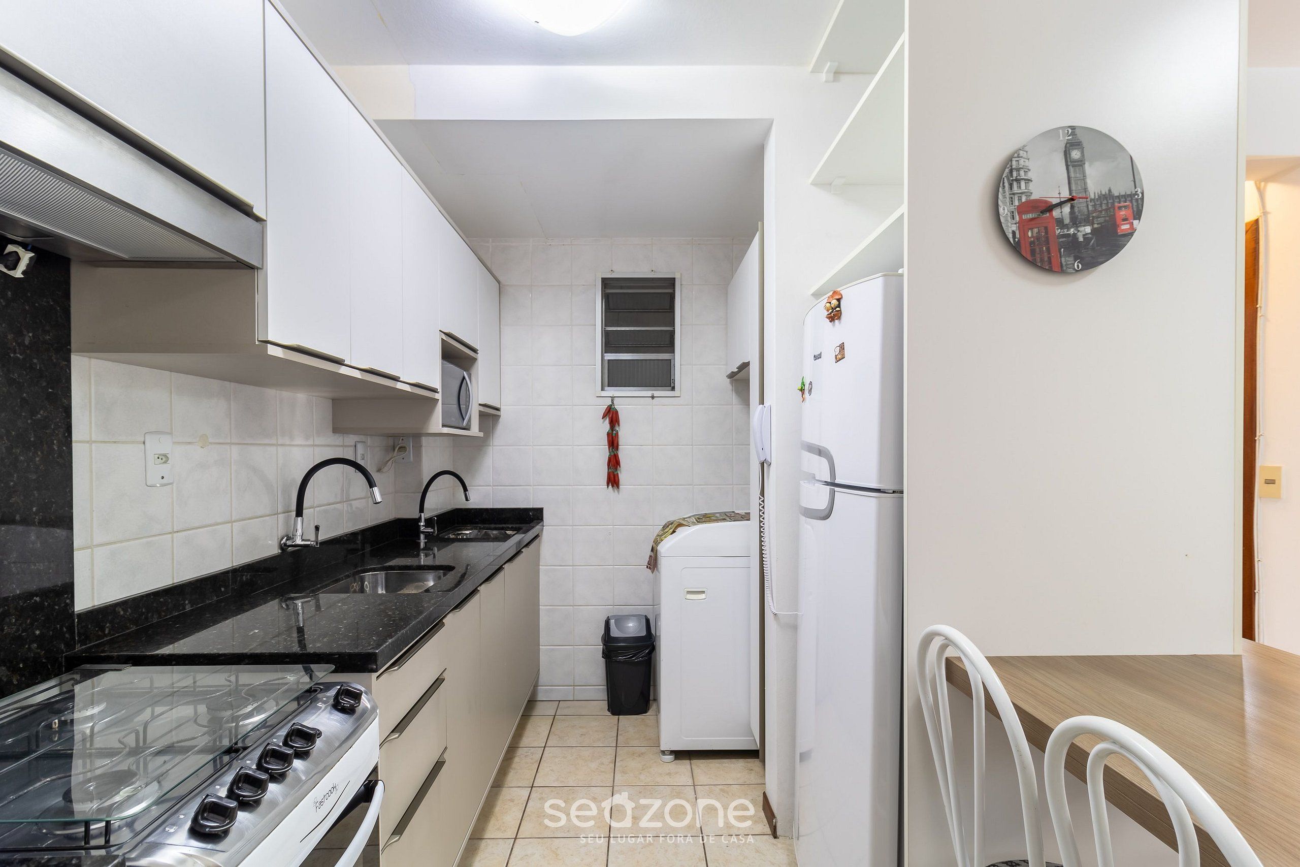 A compact kitchen with white cabinets, a black countertop, a gas stove, a small window, a trash bin, and a refrigerator.