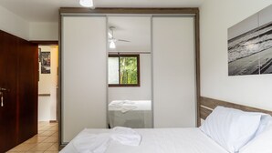 Un dormitorio con cama, armario, ventilador de techo, ventana y un cuadro en la pared.