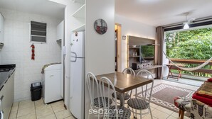 Cocina compacta con refrigerador, pequeña ventana y basurero. Hay un comedor con mesa y sillas, y una hamaca afuera.