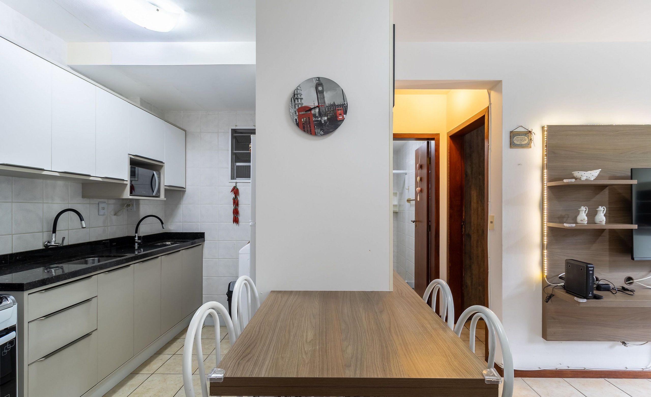 Uma cozinha moderna com armários brancos, uma mesa de jantar de madeira e um relógio na parede.