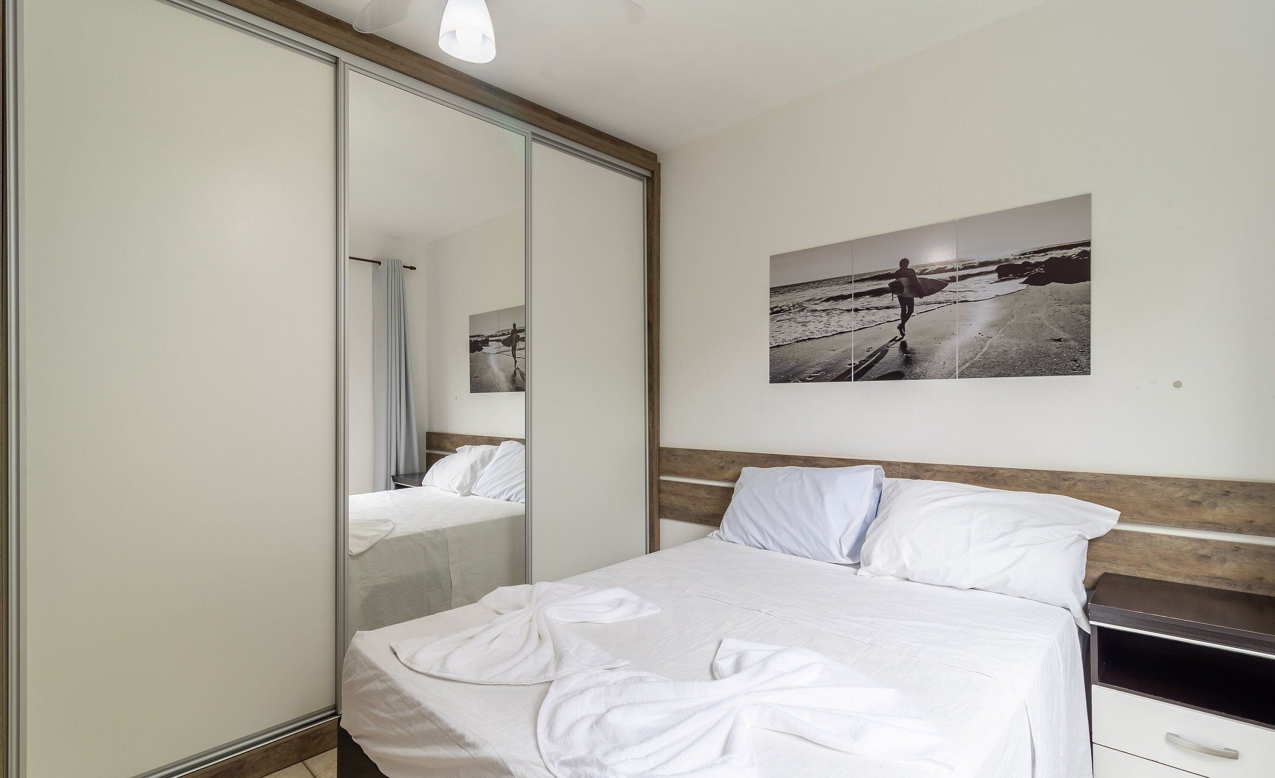 A bedroom with a bed, a bedside table, a mirror, and a wall-mounted picture.