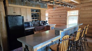 A rustic kitchen with wooden cabinets, a black refrigerator, a sink, and a bar area with stools.