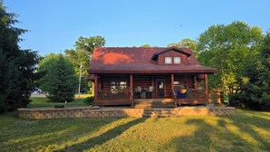 A log cabin with a porch, surrounded by a well-maintained lawn and trees.