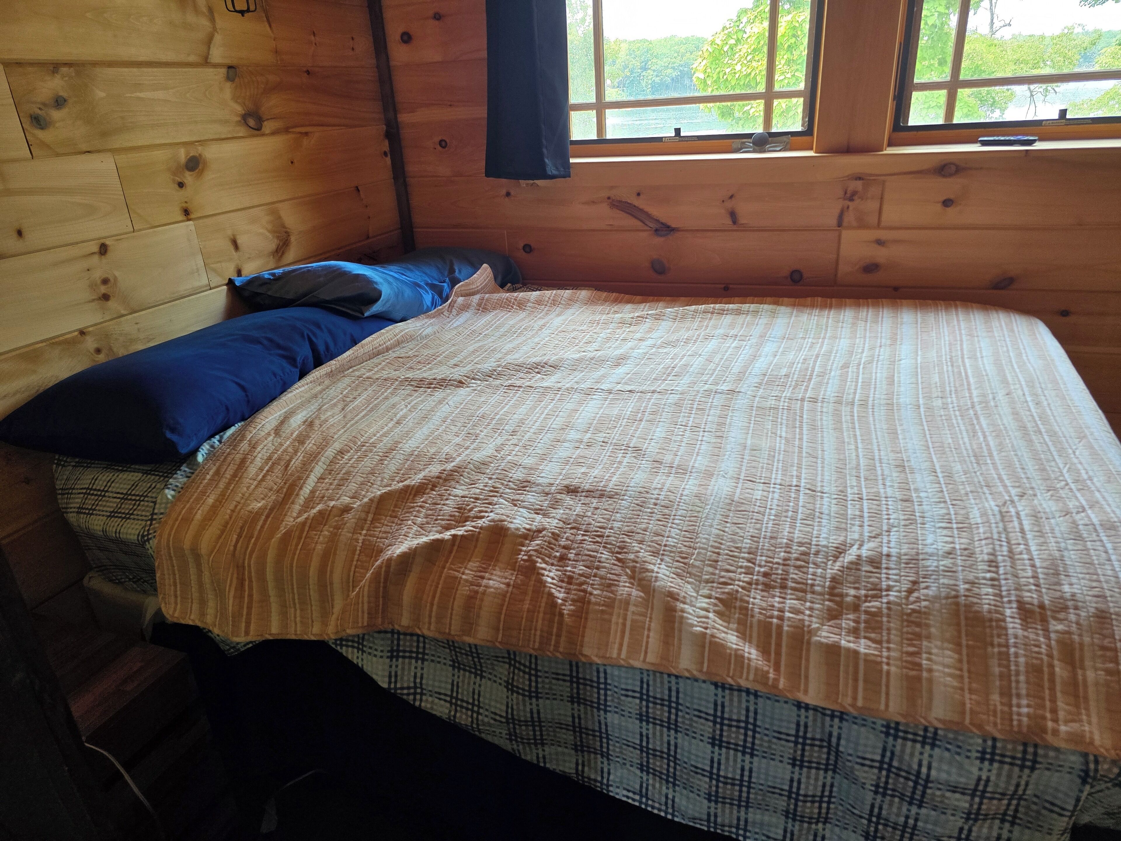 Dormitorio de cabaña de madera con cama, una ventana y vistas al verdor exterior.