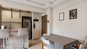 A modern kitchen with marble countertops, a built-in oven, and a refrigerator. There are two bar stools and a dining table with a checkered tablecloth. - Beautiful apt w Modern Design 400m/udesc - Abz302 (Florianópolis)