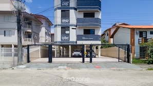 A multi-story residential building with a gated entrance, a covered parking area, and a visible sign indicating the name 'RES. AUGUSTO CESAR'. - Beautiful apt 350m From Canasvieiras Beach Ace0201 (Florianópolis)