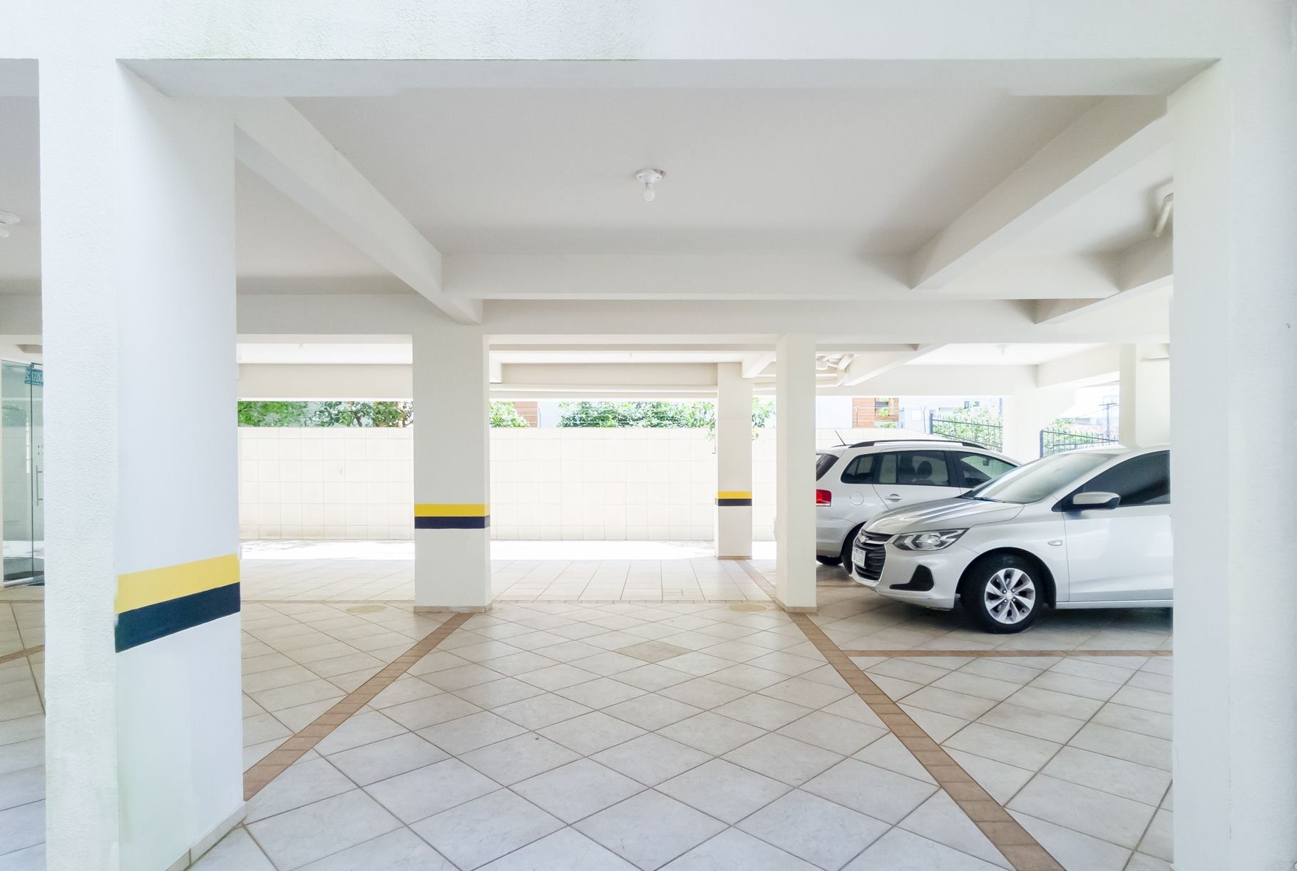 An indoor parking area with white pillars, tiled floors, and two parked cars.
