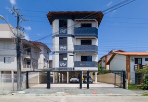 Um edifício residencial com vários andares, entrada com portão, área de estacionamento coberta e placa visível com o nome 'RES. AUGUSTO CESAR'.