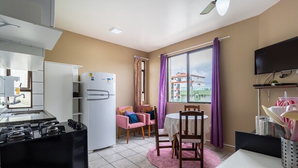 A compact kitchen with a gas stove, a white refrigerator, and a dining area with a table and chairs. - Cozy Apartment 6 Minutes From Canas Beach Acg302 (Florianópolis)