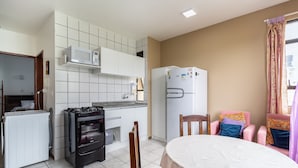 A compact kitchen with a microwave, stove, oven, and refrigerator. There is a dining table with chairs and a window with curtains. - Cozy Apartment 6 Minutes From Canas Beach Acg302 (Florianópolis)
