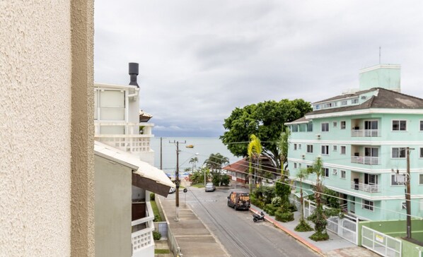 A street view with a building on the left, a green building with balconies on the right, and a clear sky. - Cozy Apartment 6 Minutes From Canas Beach Acg302 (Florianópolis)