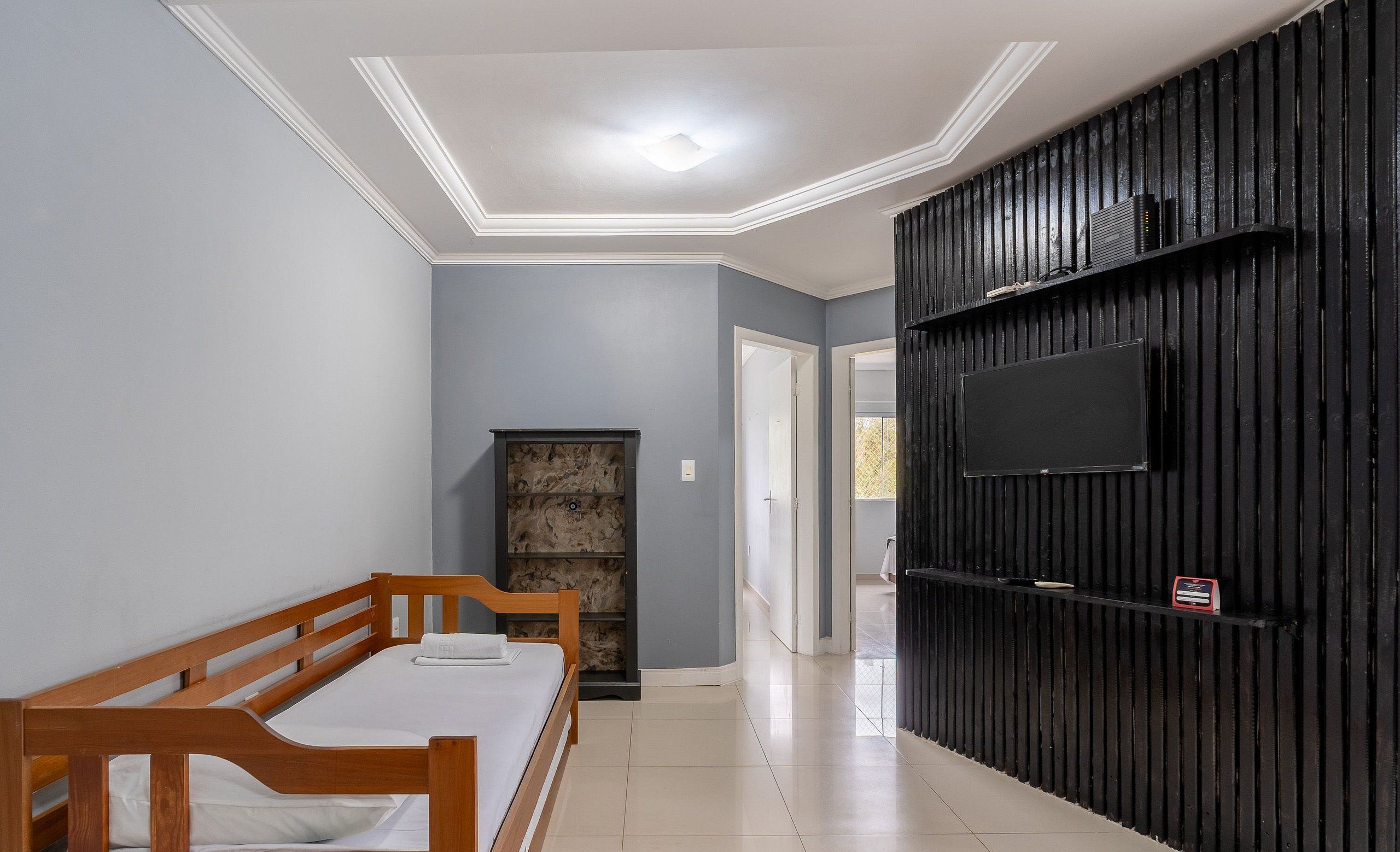 A bedroom with a wooden bed, a stone fireplace, a TV mounted on a black wall, and a tiled floor.