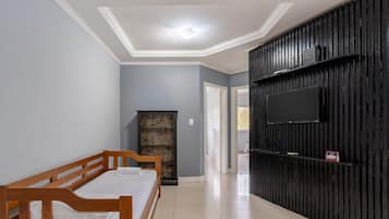 A bedroom with a wooden bed, a stone fireplace, a TV mounted on a black wall, and a tiled floor.