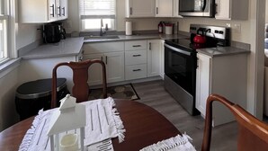 A compact kitchen with white cabinets, a microwave, and a stove. There is a dining table with chairs and a small rug.