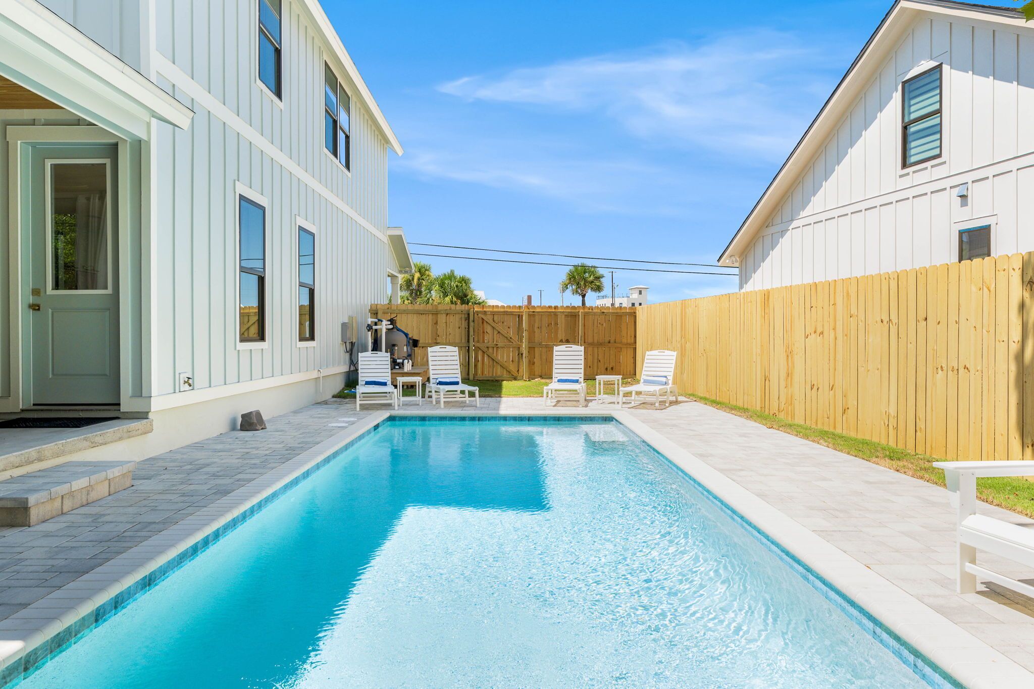 Une piscine avec des chaises longues et une clôture en bois, située dans un quartier résidentiel.